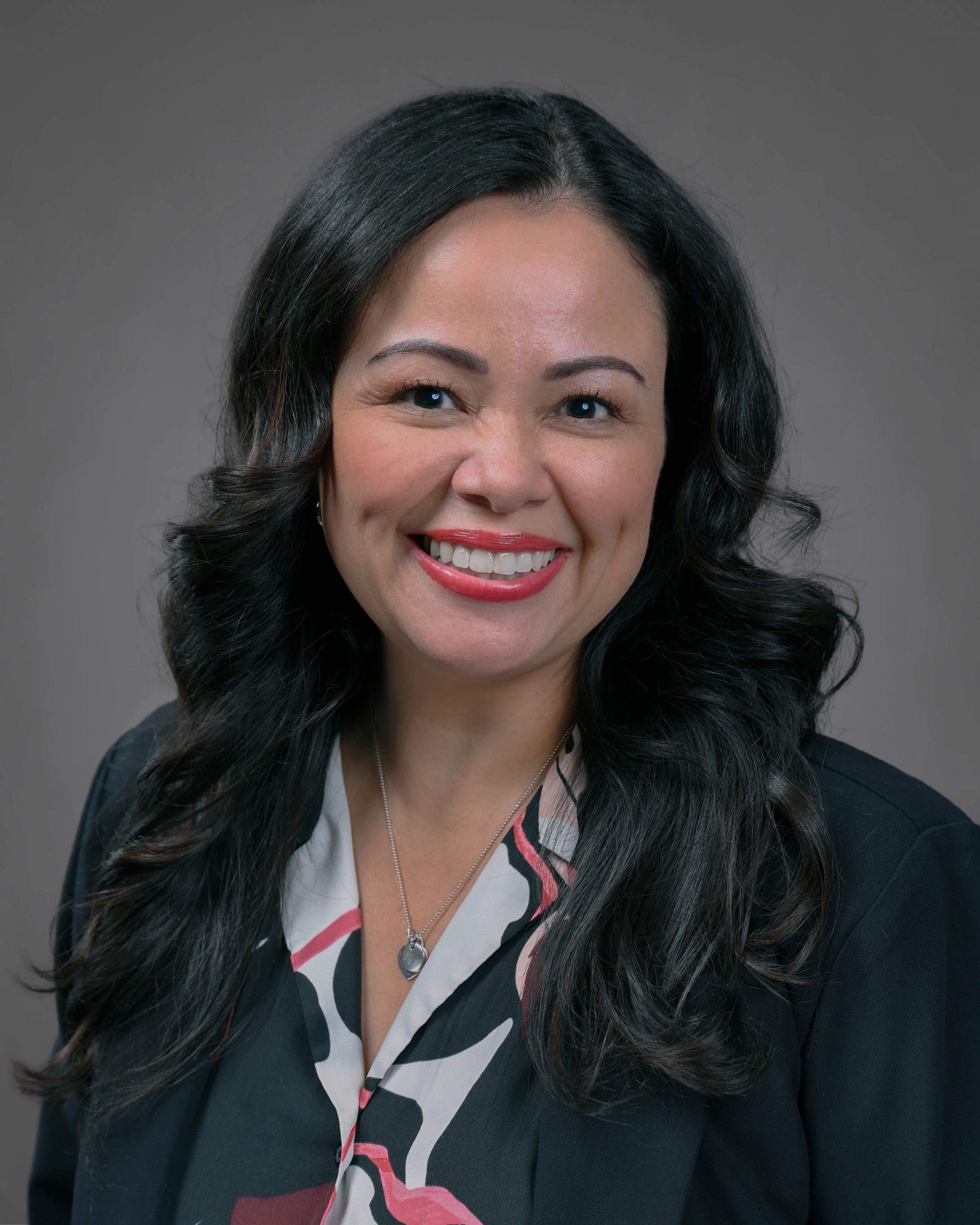 Kind looking woman with curly dark hair smiling in a dark jacket